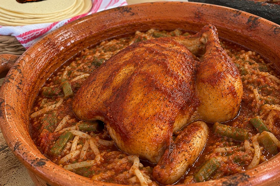 Imagen ilustrativa de pollo al horno en cazuela de barro con salsa y verduras
